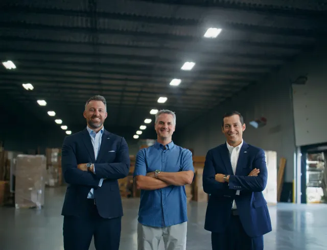 Three men standing next to each other smiling with their arms crossed
