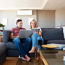 Couple in living room looking at laptop and tablet.