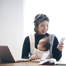 Woman with baby in carrier, using mobile phone and working